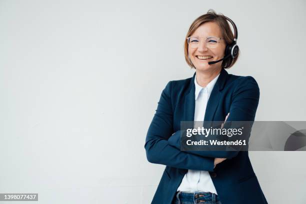 happy telecaller wearing headset standing with arms crossed against white background - hands free device foto e immagini stock