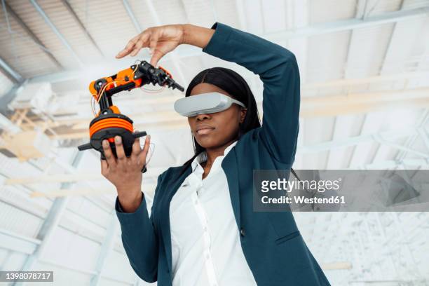 engineer wearing virtual reality simulator holding model of robotic arm in factory - stem assunto imagens e fotografias de stock