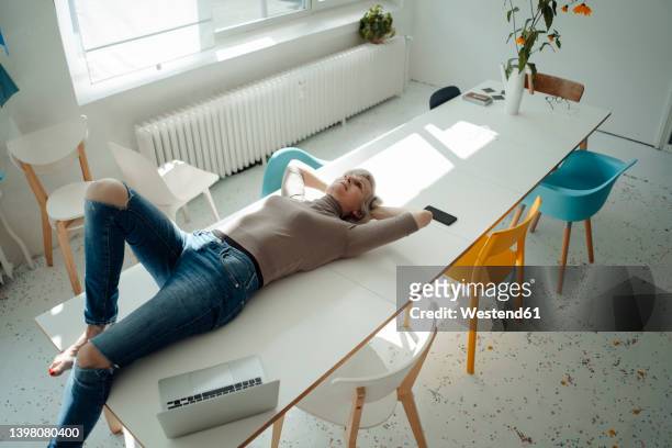 senior businesswoman with hands behind head lying on desk in office - head on table stock-fotos und bilder