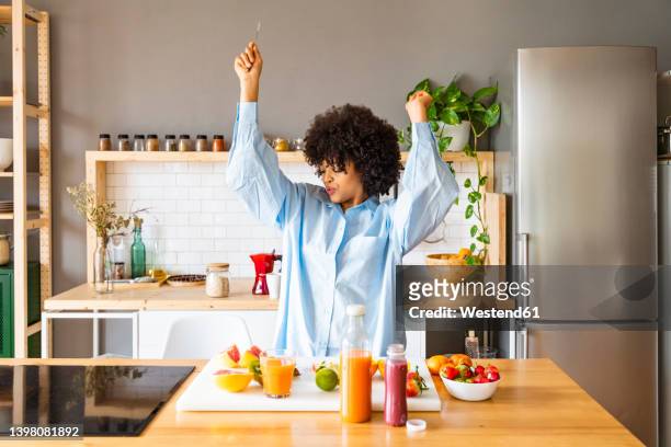 happy woman with arms raised dancing in kitchen at home - knife kitchen stock pictures, royalty-free photos & images