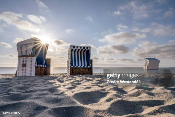 germany, schleswig-holstein, hornum, morning sun shining over empty hooded beach chairs standing on sandy beach - strandkorb stock-fotos und bilder