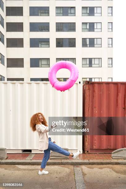 businesswoman playing with pink inflatable ring in front of building - lanzar actividad física fotografías e imágenes de stock