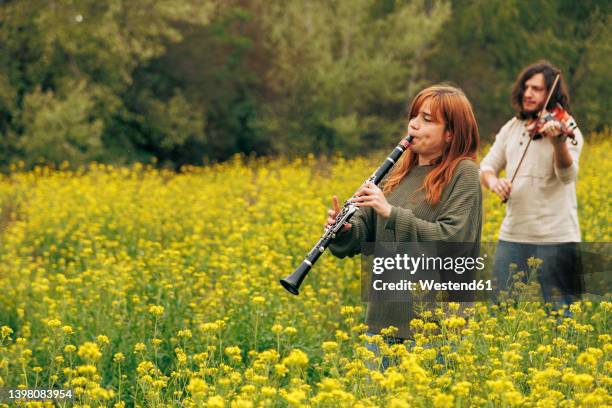 woman practicing clarinet with man playing violin walking in flower field - 木管楽器 ストックフォトと画像