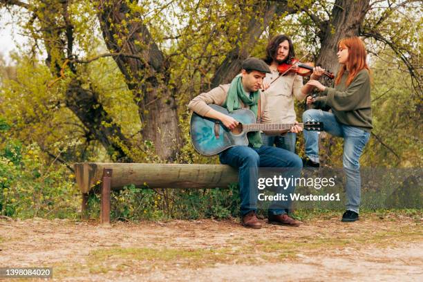 artists with musical instruments practicing near bench by tree - folk foto e immagini stock