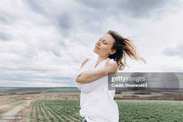 woman with eyes closed hugging self in agricultural field - hugging self stock-fotos und bilder