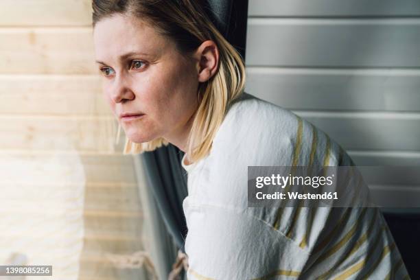 sad woman looking out of window at home - woman 38 stockfoto's en -beelden