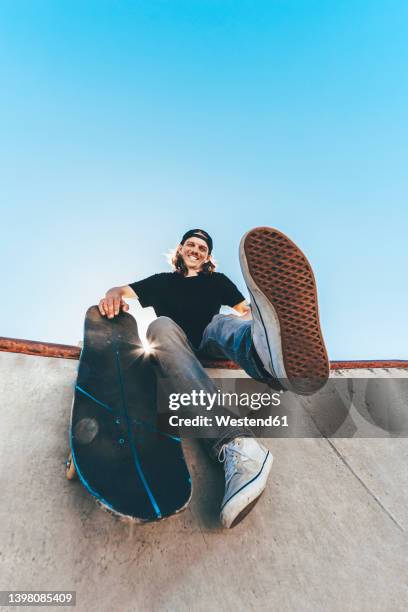 happy man with skateboard sitting at skateboard park - soles pose stockfoto's en -beelden