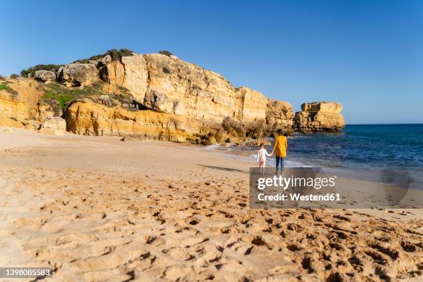 mother and daughter walking on shore at beach - albufeira beach stock pictures, royalty-free photos & images