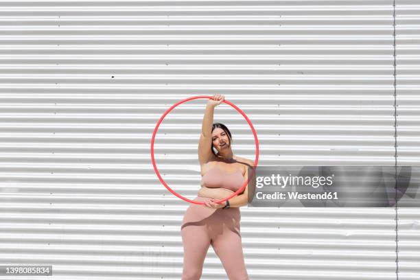 curvy woman holding plastic hoop standing in front of corrugated wall - jogar ao arco imagens e fotografias de stock