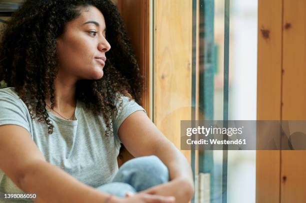 young woman looking through window at home - introspektion stock-fotos und bilder