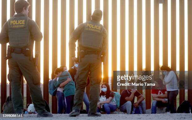 Border Patrol agents keep watch as immigrants wait to board a U.S. Border Patrol bus to be taken for processing after crossing the border from Mexico...