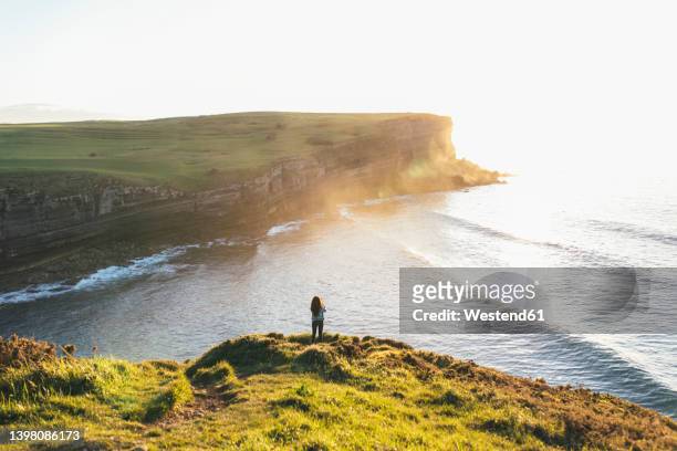 young woman standing at coast looking at sea - cantabria stock pictures, royalty-free photos & images