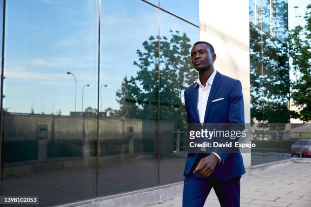side view of a black businessman walking near a glass building - formal businesswear stock pictures, royalty-free photos & images