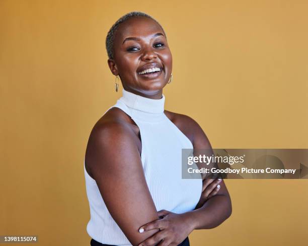 young businesswoman laughing with her arms crossed on a yellow background - black woman arms crossed stock pictures, royalty-free photos & images