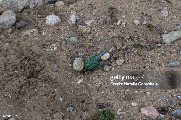 old detonated grenade on rocky soil. place of military battles. explosive equipment on dirty ground - hand grenade stock pictures, royalty-free photos & images