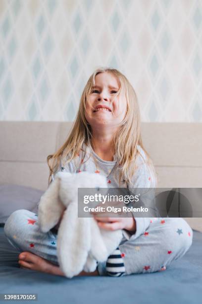 little girl crying in nightwear, sitting with crossed legs and hugging a stuffed toy. child abuse, family divorce sadness - broken toy stock pictures, royalty-free photos & images