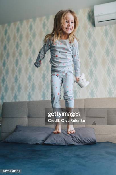 morning activity of fair-haired little girl, bouncing and jumping on her bed on the weekend. - pajamas stock pictures, royalty-free photos & images