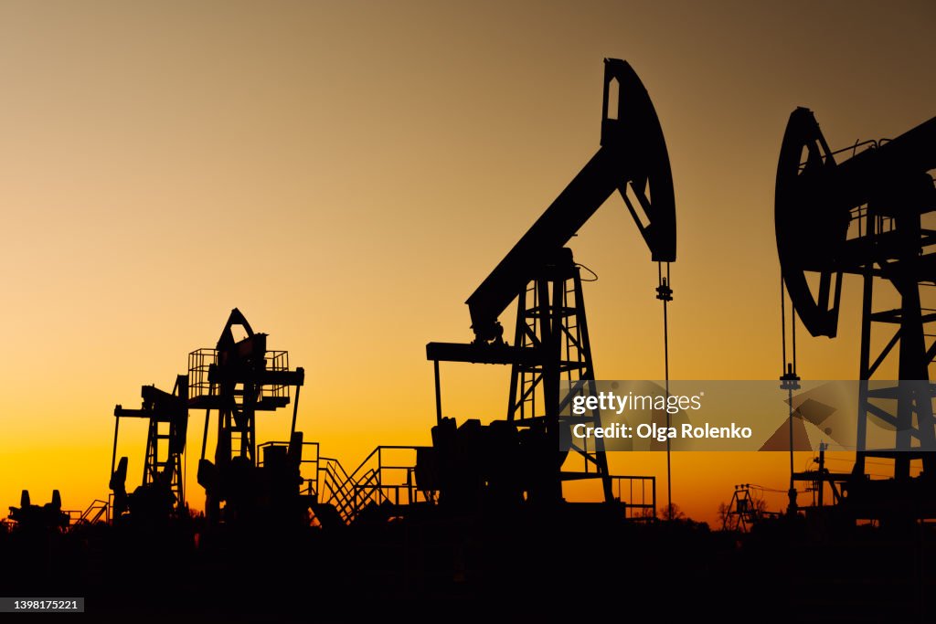 The silhouette of two oil pumps on a beautiful yellow sunset sky. Oil production well in Siberia