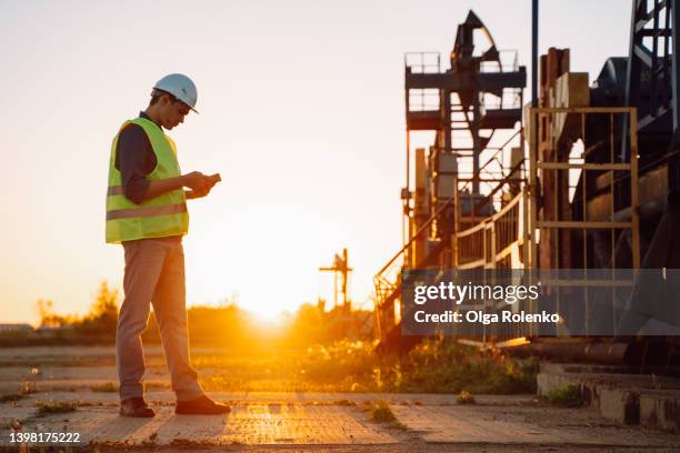 chemical technical engineer inspecting oil and gas equipment with mobile information tablet near oil jack pump platform - oil rig worker stock pictures, royalty-free photos & images