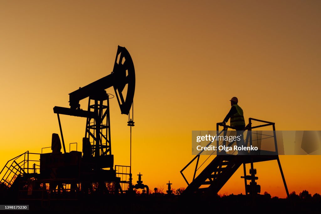 The silhouette oil pumps or nodding donkeys against dusk sky. Oil and gas production, copy space