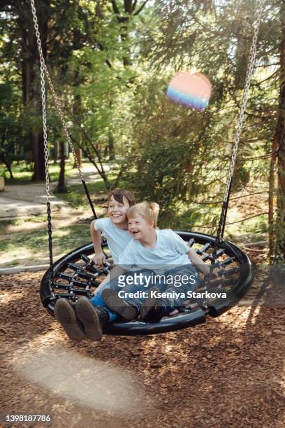 a little european fair-haired boy with down syndrome and his older brother swing on a swing in the park - fair haired boy stock-fotos und bilder