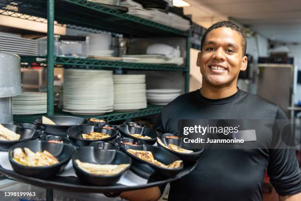 headshot of a smiling latin afro-caribbean waiter holding a tray with food - latin america stockfoto's en -beelden