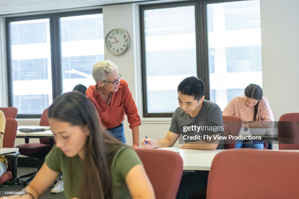 Teacher Helping High School Student With Assignment In Class High-Res ...