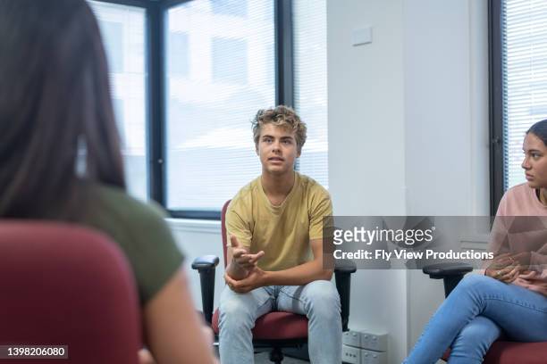 teenage boy sharing life experience with peers in group therapy - teen group therapy stock pictures, royalty-free photos & images
