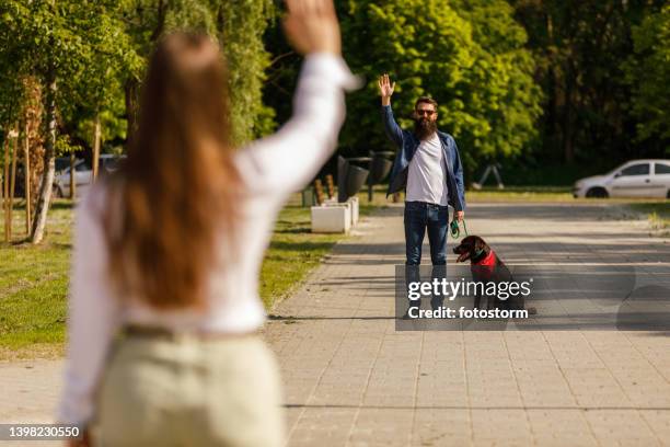 couple meeting at the park to walk the dog, standing apart and waving at each other - dog greeting stock pictures, royalty-free photos & images