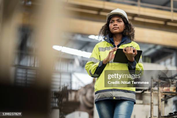 creating a culture of quality and safety in manufacturing industry.  low angle view of a female african american engineer holding a digital tablet while standing in the factory surrounded by machinery. - black american culture stock pictures, royalty-free photos & images