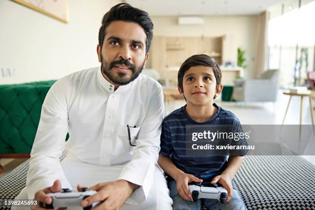 saudi father and son playing video game at home - thawb stock pictures, royalty-free photos & images