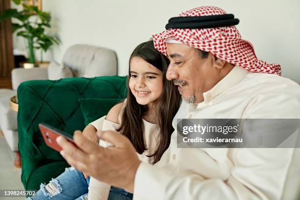 mature saudi man and granddaughter taking selfie at home - saudi people stock pictures, royalty-free photos & images