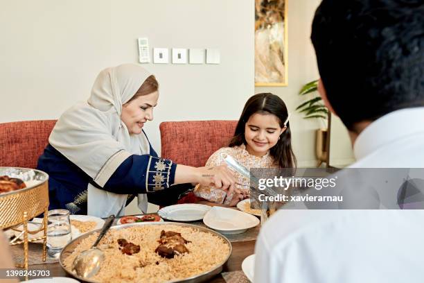 abuela saudita sirviendo kabsa al niño durante la comida - arab family eating fotografías e imágenes de stock