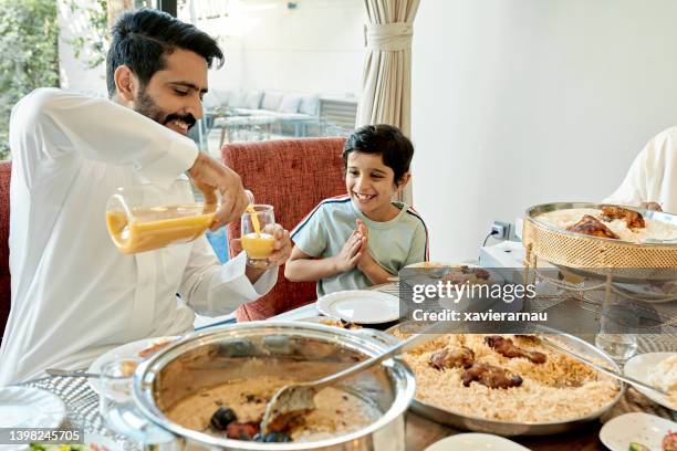 padre mediorientale che serve succo di frutta al figlio sorridente - generations arab foto e immagini stock