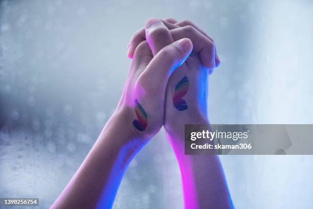 close up female hands holding hands  lesbian female couple lovers with lgbt butterfly rainbow  tattoo. concept of  lgbtiqa+ - revolutionary war flag stock-fotos und bilder