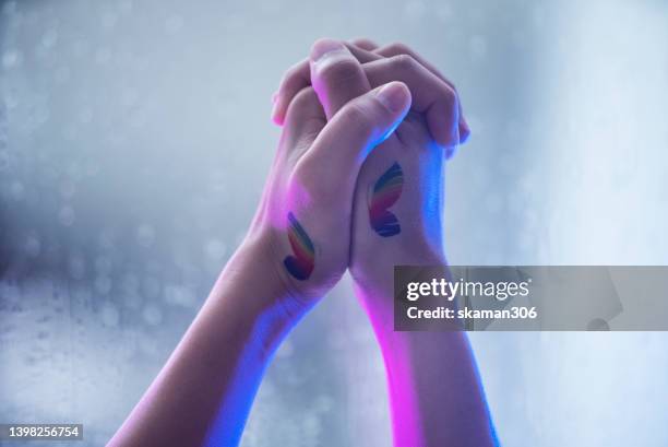 close up female hands holding hands  lesbian female couple lovers with lgbt butterfly rainbow  tattoo. concept of  lgbtiqa+ - gay flag stockfoto's en -beelden