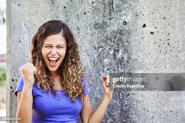beautiful young woman laughs and punches the air exultantly in celebration: she's a winner! - punching the air stock pictures, royalty-free photos & images