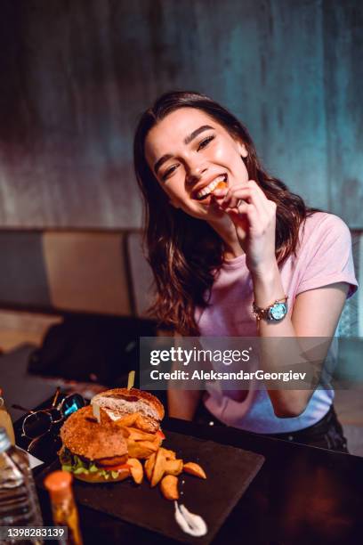 cute female tasting potato while having lunch at bar - gefrituurde kip stockfoto's en -beelden