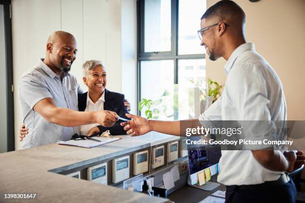 smiling mature couple giving hotel reception their cardkey - checkout 個照片及圖片檔