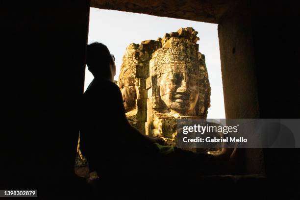 silhouette of man sitting with views of bayon temple - bayontempel stockfoto's en -beelden