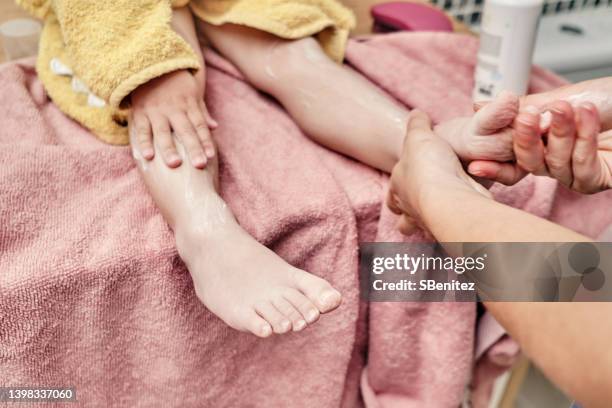 mother rubbing lotion on her little daughter's leg after a bath - eczema child stock-fotos und bilder