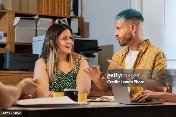 medium shoot of a two young coworkers talking around a table indoors - hair color stock pictures, royalty-free photos & images