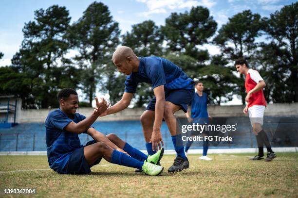 athlete supporting injured player on soccer field - injured football player stock pictures, royalty-free photos & images