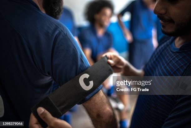 futbolista ayudando al capitán del equipo a ponerse el brazalete - capitán del equipo fotografías e imágenes de stock