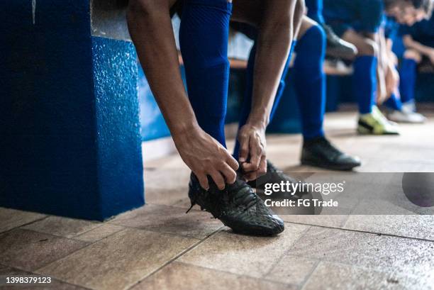 giocatore di calcio che lega i lacci delle scarpe mentre si prepara per la partita nello spogliatoio - spogliatoio foto e immagini stock