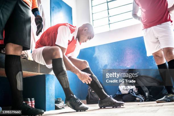 ロッカールームで試合前に靴ひもを結んでいるサッカー選手 - シンガード ストックフォトと画像