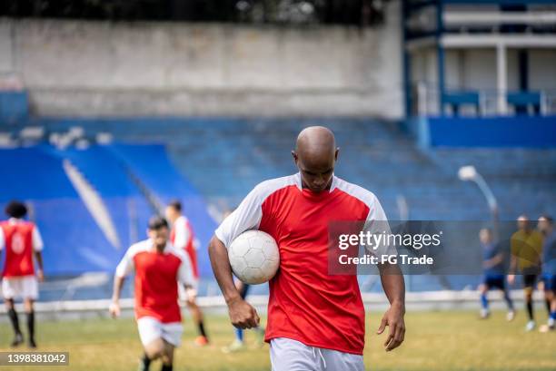 soccer player holding soccer ball while leaving the field - sad football player stock pictures, royalty-free photos & images