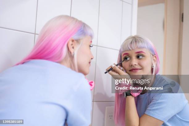 young woman with pink hair applying make up in the bathroom mirror - hair coloring stock pictures, royalty-free photos & images