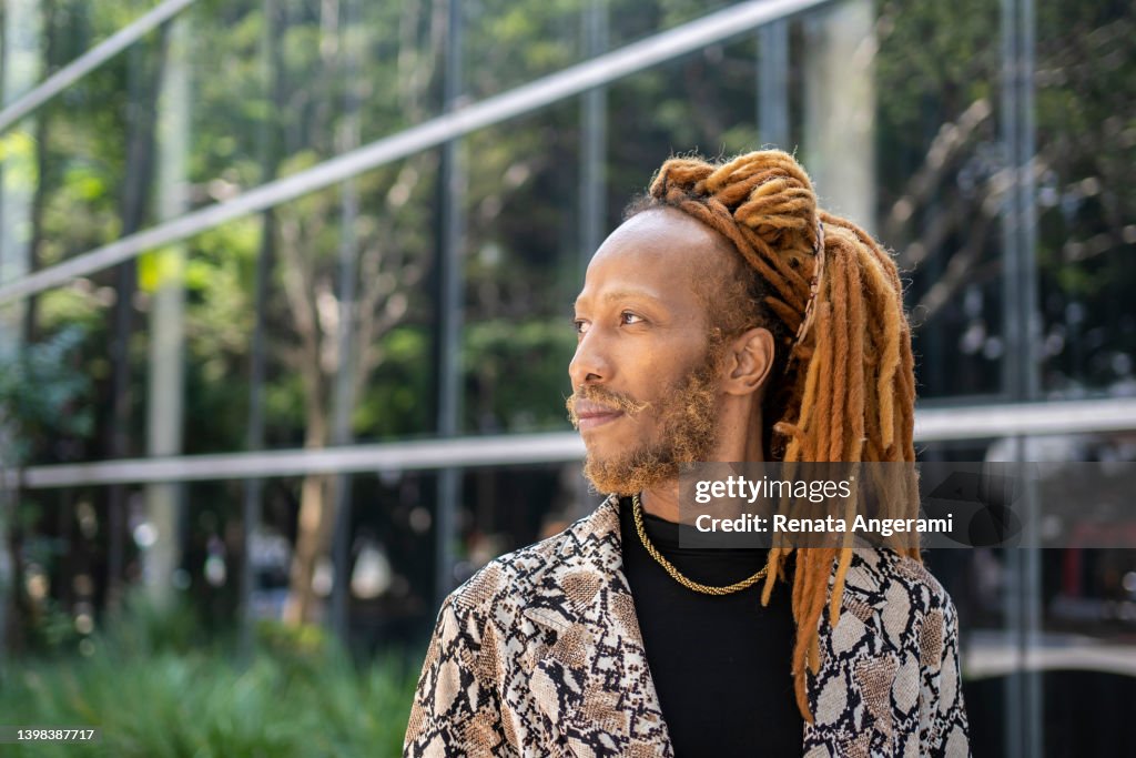 Portrait of black man with dreadlocked hair with smart phone outside the office building