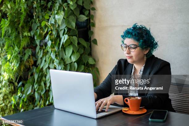 mujer joven con el pelo verde trabajando en la computadora en la cafetería - dyed red hair fotografías e imágenes de stock